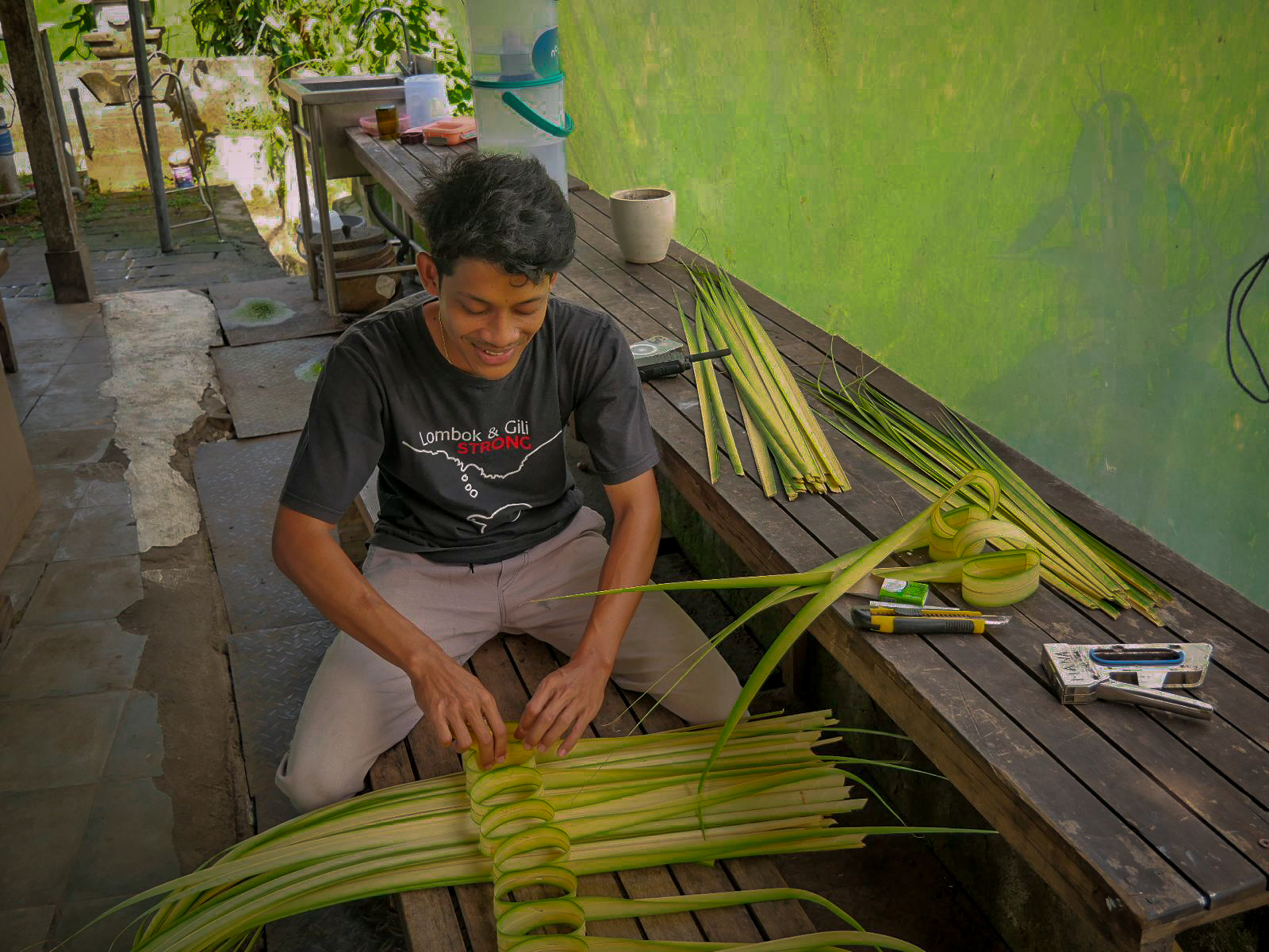 ragazzo balinese mentre costruisce un penjor con foglie di palma verdi durante il Galungan