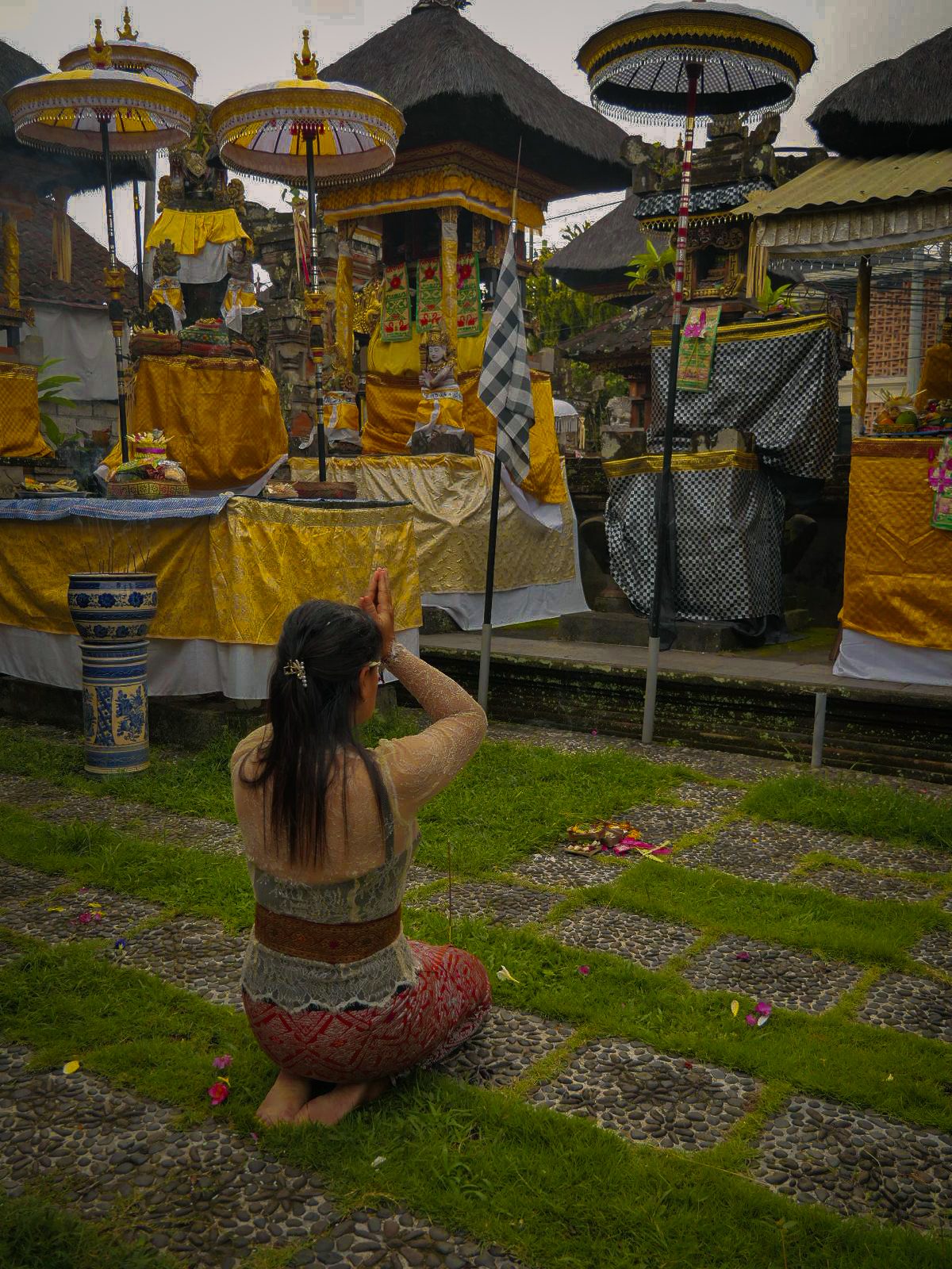 donna balinese vestita con abiti tradizionali seduta in preghiera all'interno di un tempio